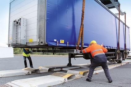Two workers positioning a swap body onto a trailer.