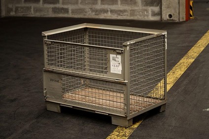 Empty metal mesh storage container on a pallet in an industrial warehouse area.