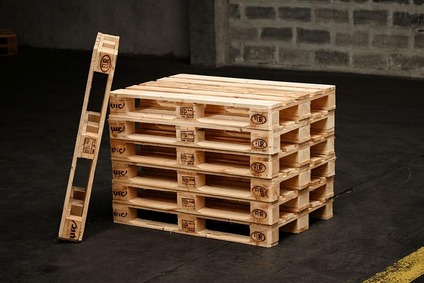Stack of EUR wooden pallets with one pallet standing upright in an industrial warehouse.