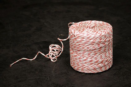 Roll of red-and-white rope with a loose end on a dark industrial surface.