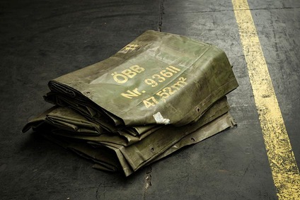 Folded green railway wagon cover marked “ÖBB” stacked on an industrial floor.