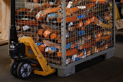 Gitterbox mit orangefarbenen Zurrgurten, bewegt mit einem Hubwagen in einem Lagerbereich.