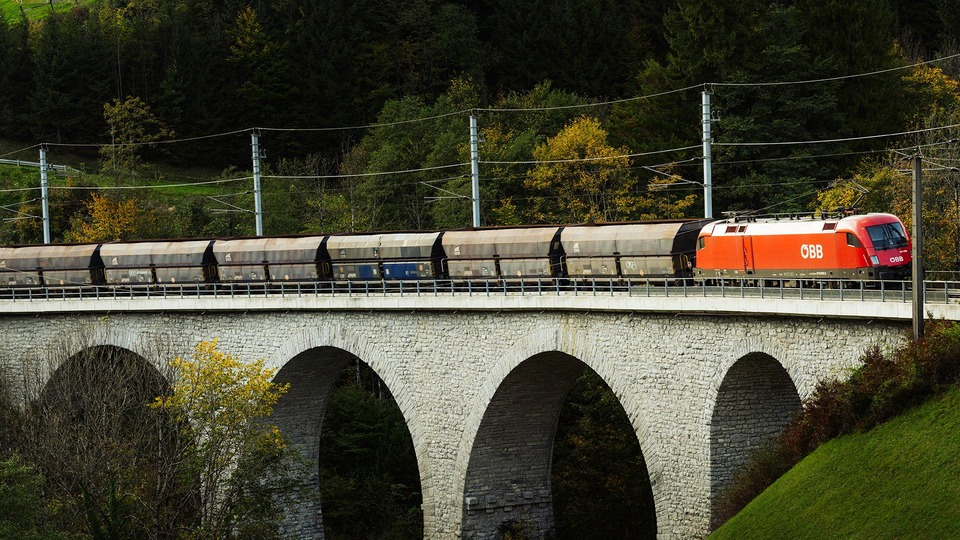 ÖBB freight train crossing a stone arch bridge in a forest landscape