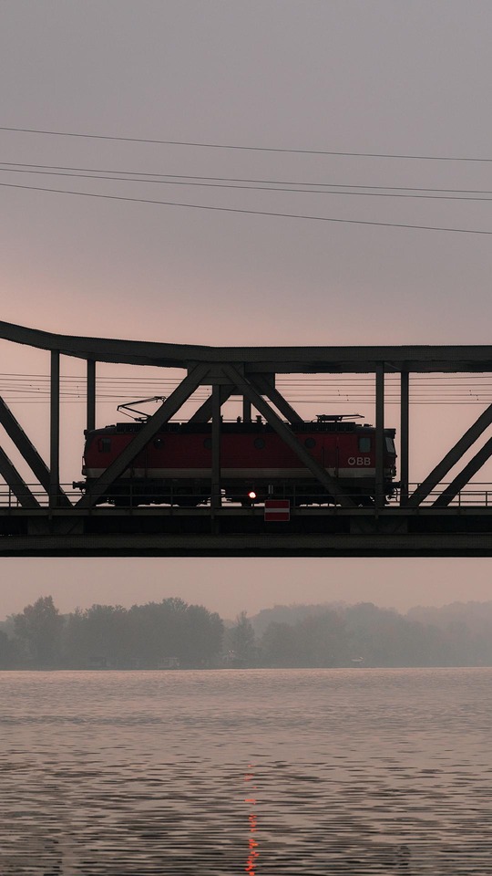 ÖBB locomotive crossing a steel bridge over a river at dusk