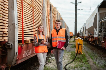 Two apprentices in safety vests standing beside freight wagons in a rail yard