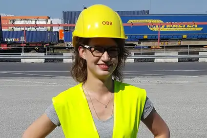 Logistikerin mit Schutzhelm und Warnweste an einem Bahnterminal