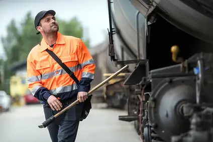 Wagenmeister steht neben einem Güterwagen und hält ein Werkzeug