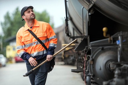 Rail yard inspector standing beside a freight wagon holding a tool