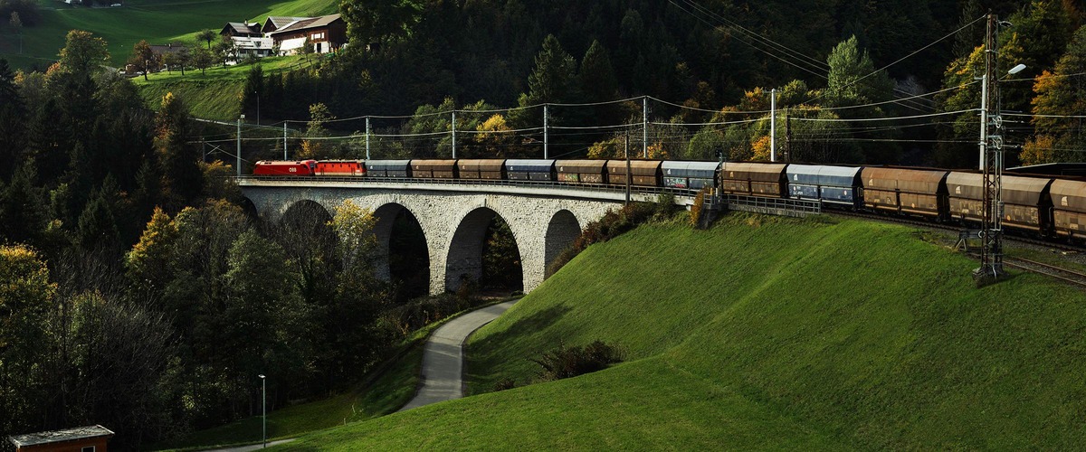 Güterzug fährt über eine steinerne Eisenbahnbrücke in hügeliger Landschaft