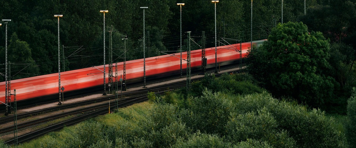 Red train in motion on illuminated tracks beside trees