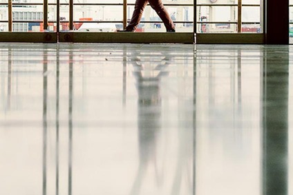 Person geht durch einen verglasten Gang mit Spiegelung auf dem polierten Boden