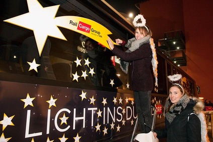 Zwei Frauen schmücken einen Rail Cargo Group Zug mit Weihnachtslichtern und Sternen bei einem festlichen Abendevent