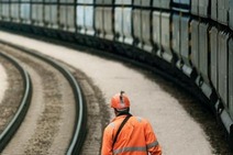 Bahnarbeiter geht entlang einer Kurve neben einem vorbeifahrenden Güterzug