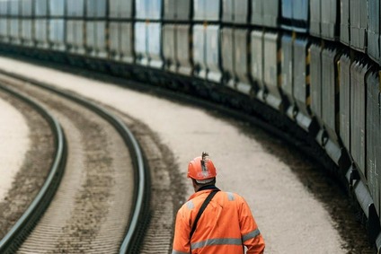 Bahnmitarbeiter in Schutzkleidung geht neben einem langen Güterzug auf einer Kurve