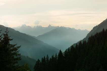 Neblige Alpenlandschaft mit gestaffelten Berggipfeln und bewaldetem Tal im Abendlicht