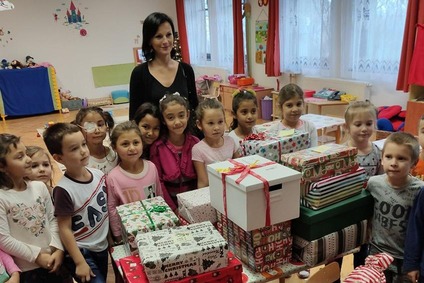 Lehrerin und Kinder im Klassenraum versammelt um einen Tisch mit eingepackten Weihnachtsgeschenken