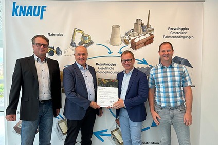 Vier Männer halten ein Nachhaltigkeitszertifikat vor einer Knauf-Recycling-Grafik