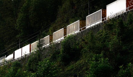 Containerzug fährt auf einer Bahnstrecke entlang eines bewaldeten Hanges