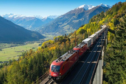 ÖBB-Güterzug mit Containern fährt durch eine Alpenlandschaft auf einer Hochbahnstrecke