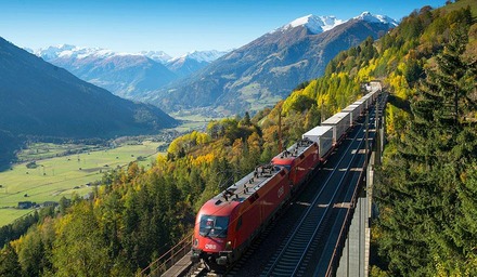 Containerzug der ÖBB fährt auf einer Bahnstrecke durch eine Berglandschaft der Alpen