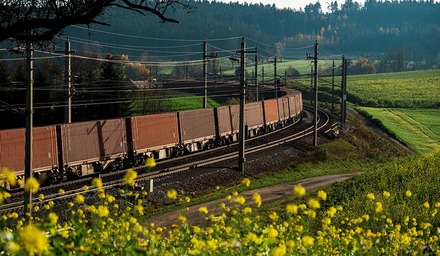 Güterzug auf kurviger Bahnstrecke durch grüne Landschaft mit Feldern