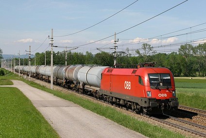 ÖBB Lokomotive zieht langen Kesselwagenzug durch grüne Felder