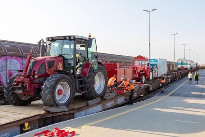 Landmaschinen werden von Mitarbeitenden auf Flachwagen eines Güterzugs verladen