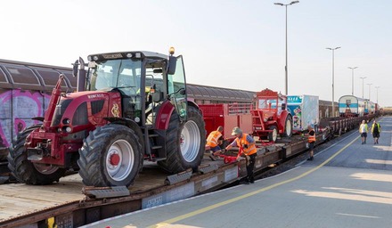 Traktor und Landmaschinen auf Güterwagen verladen, Mitarbeitende sichern die Ladung
