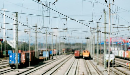 Güterzüge und Container in einem Rangierbahnhof mit Oberleitungen, leicht unscharf dargestellt