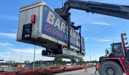 Reachstacker hebt einen Container an einem Terminal auf einen Bahnwagen