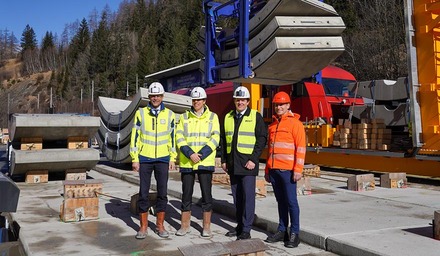Vier Vertreter auf einer Baustelle mit Schutzhelmen und Warnkleidung vor Bahninfrastruktur