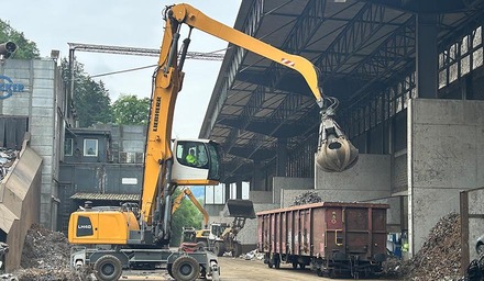 Umschlag von Metallschrott mit Bagger in einen Güterwagen in einer Recyclinganlage