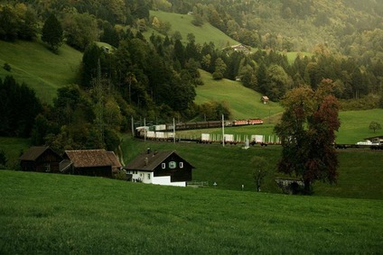 ÖBB Güterzug der Rail Cargo Group fährt durch eine hügelige Landschaft mit Wiesen, Wäldern und Bauernhäusern