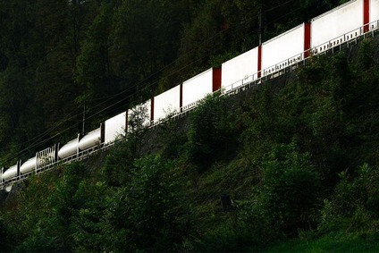 Intermodaler Güterzug mit Containern fährt auf einer Bahnstrecke durch eine bewaldete Hanglandschaft