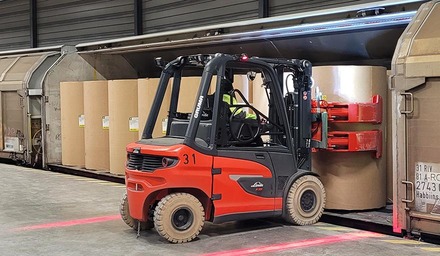 Gabelstapler lädt große Papierrollen in einen Güterwagen im Logistikterminal