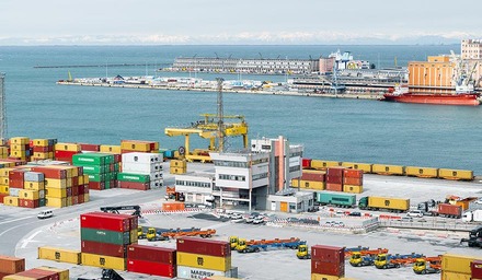 Containerterminal in einem Seehafen mit gestapelten Containern, Kränen und Frachtschiffen im Hintergrund