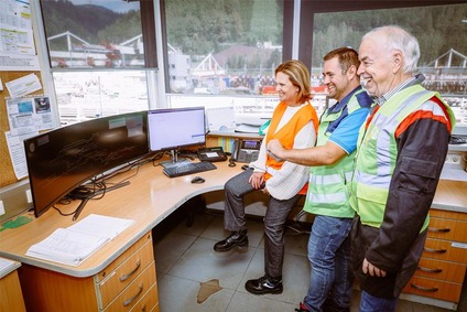 Drei Mitarbeitende mit Warnwesten betrachten Monitore in einer Leitstelle mit Blick auf eine Industrieanlage