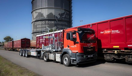 LogServ-Lkw mit MOBILER-System und Schüttgutbehälter neben einem Güterzug der Rail Cargo Group