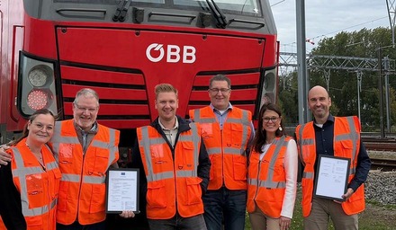 Sechs Mitarbeitende der Rail Cargo Group mit Warnwesten stehen vor einer ÖBB-Lokomotive und halten Zertifikate
