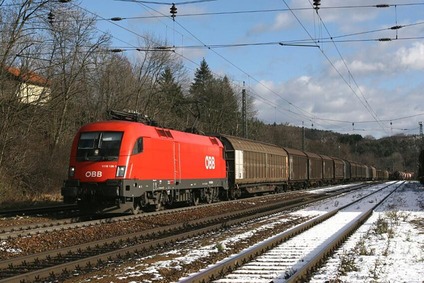 Roter ÖBB-Güterzug mit Elektrolokomotive und Güterwagen auf einer Bahnstrecke in winterlicher Landschaft