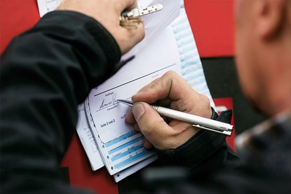 Person unterschreibt ein offizielles Dokument auf einem Klemmbrett mit einem Stift.