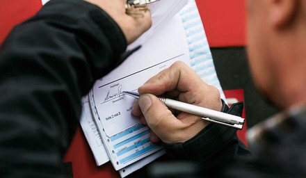 Person unterschreibt ein offizielles Dokument auf einem Klemmbrett mit einem Stift.