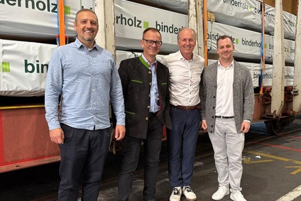 Vier Männer stehen gemeinsam vor einem Güterwaggon mit verpackten Holzprodukten.