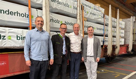 Vier Männer stehen gemeinsam vor einem Güterwaggon mit verpackten Holzprodukten.