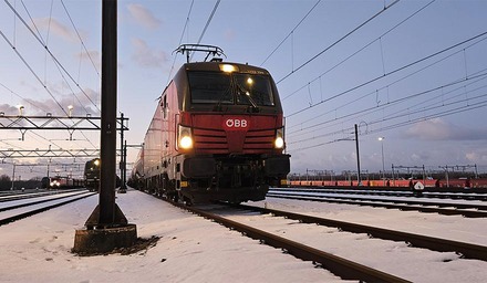 Rote ÖBB Vectron-Elektrolok im verschneiten Rangierbahnhof bei Dämmerung, mit Scheinwerfern.