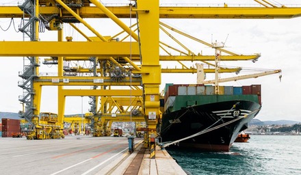 Frachtschiff am Containerterminal mit großen Kränen und gestapelten Containern am Hafen