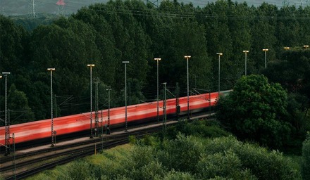 Langer Güterzug auf Bahnstrecke umgeben von Wald und Oberleitungen im ländlichen Gebiet