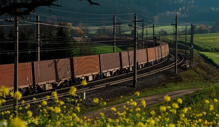 Intermodaler Güterzug auf kurviger Strecke, umgeben von Wiesen und ländlicher Umgebung