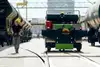 Worker in yellow helmet with remote control beside green shunting unit between freight wagons.