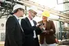 Three professionals in safety helmets reviewing a smartphone at an industrial site.
